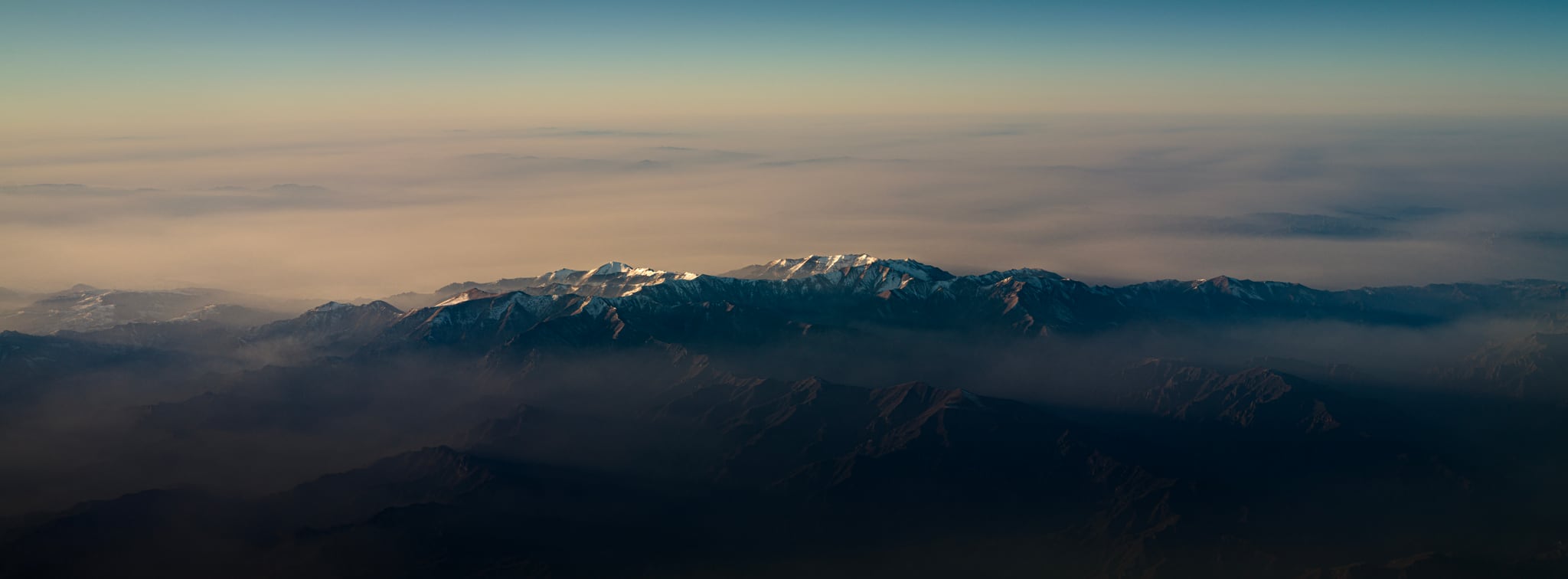A wide mountain ridge with snow along its peaks rises above a low blanket of cloud.