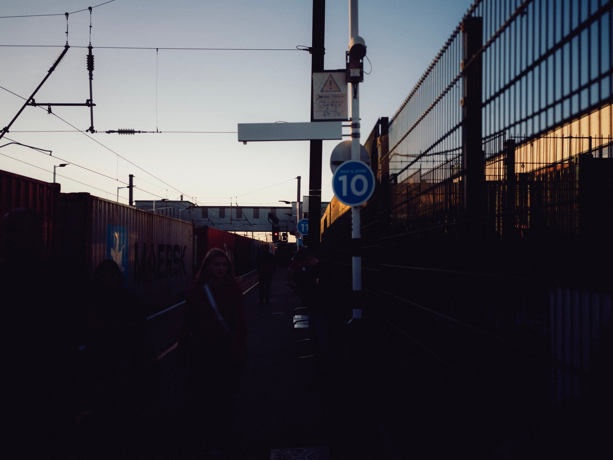 Railway tracks and overhead cables pass a glass-fronted building in low evening light.
