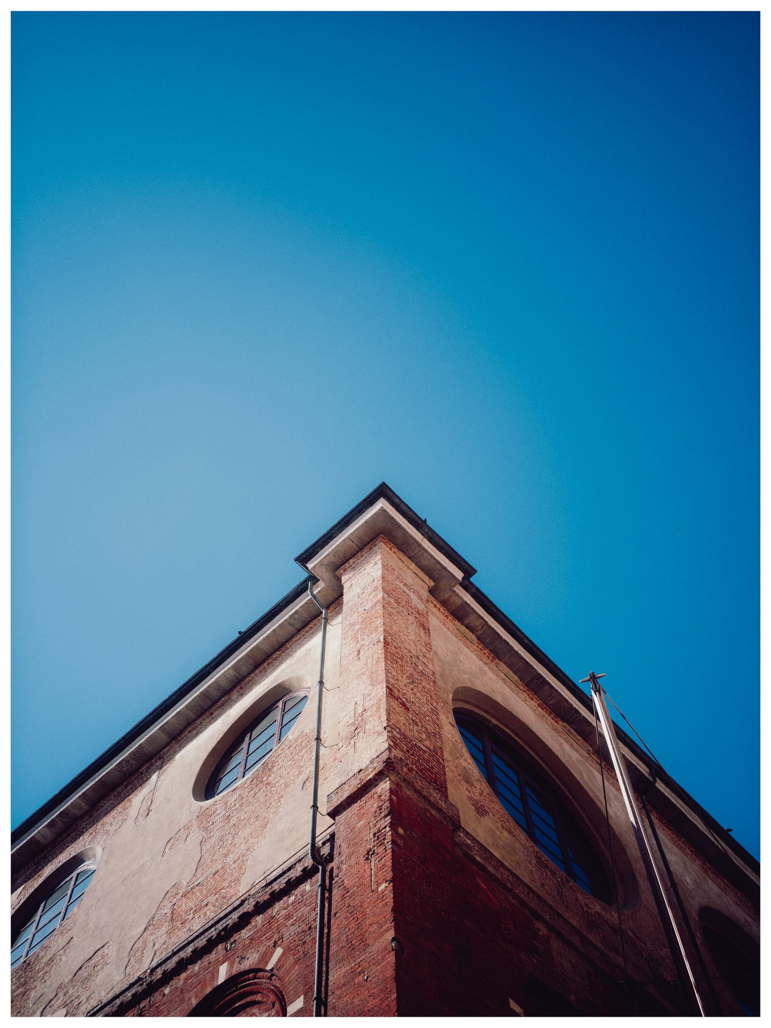 The corner of a red-brick building points into a clear blue sky in an upward view.