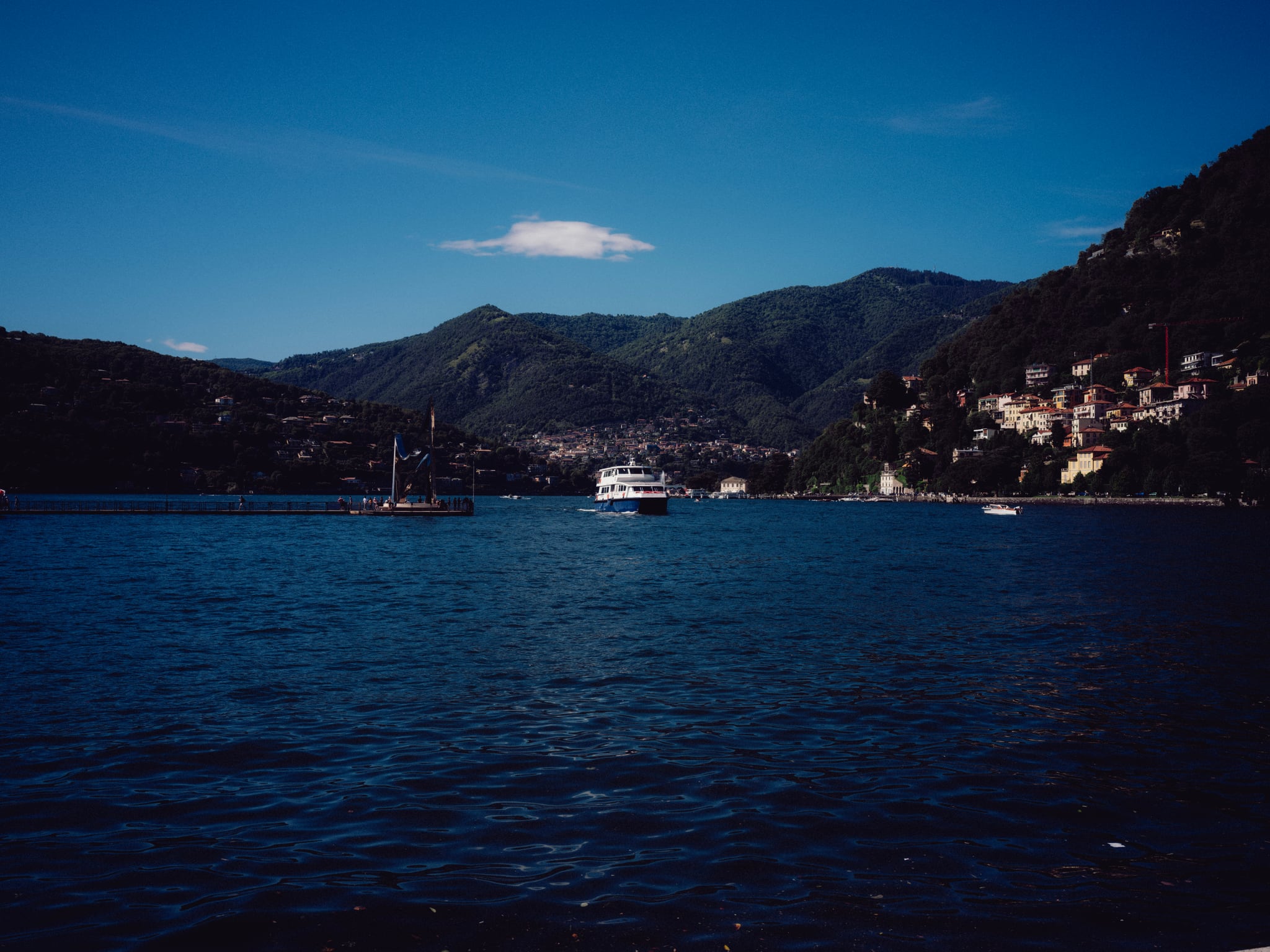 Dark blue lake water stretches toward mountains and hillside buildings beneath a clear sky.