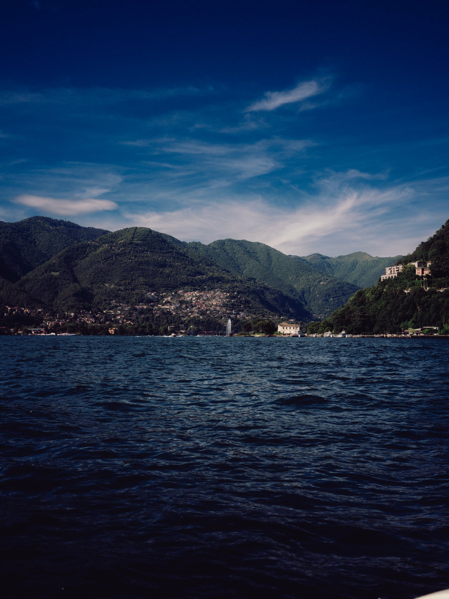 Rippling blue water fills the foreground below green mountain slopes and wisps of white cloud.