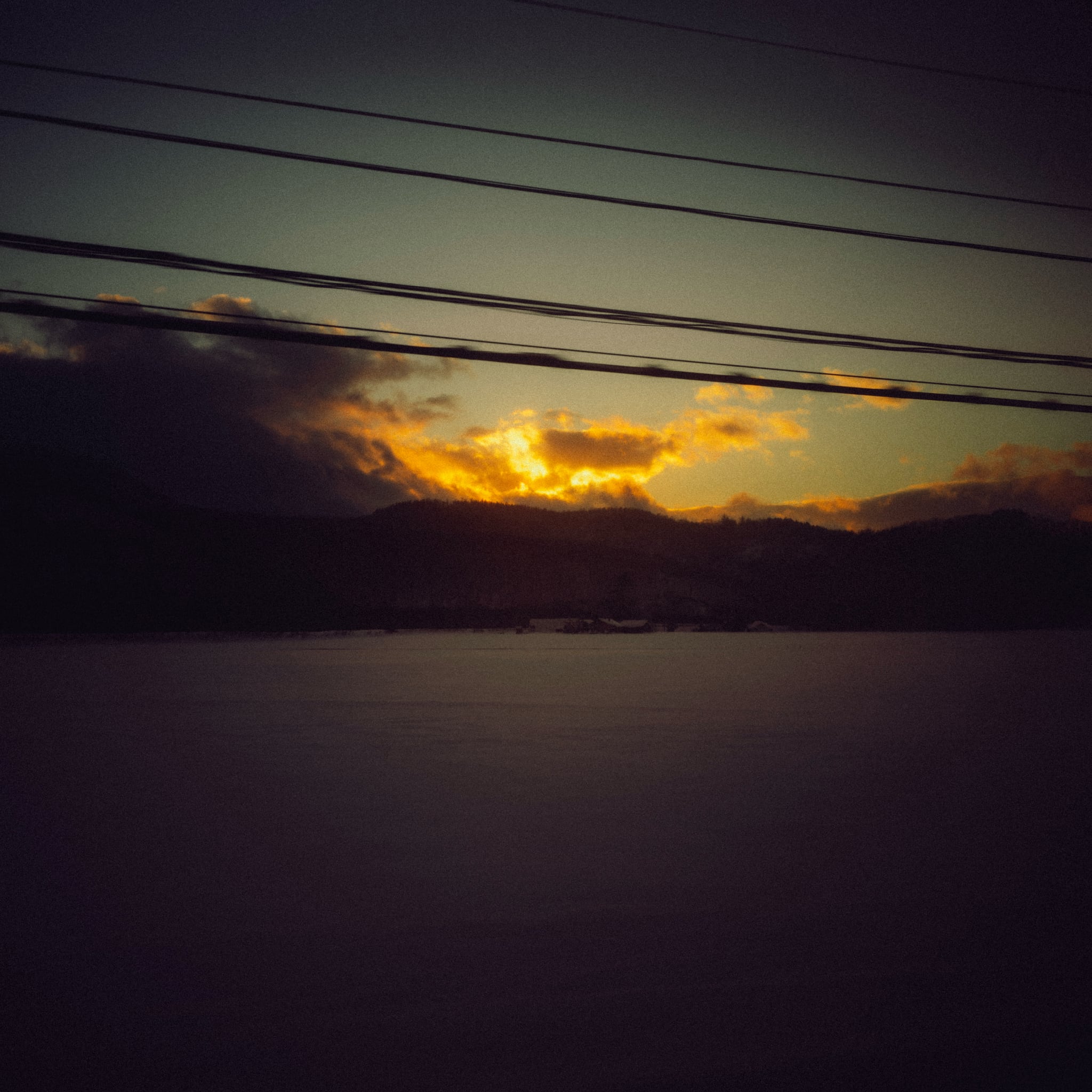 Overhead wires cut across a dark sky and a bright orange sunset above water.