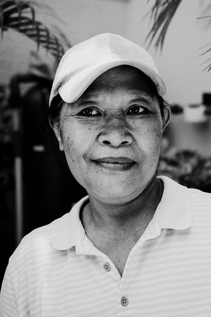 A close black-and-white portrait of a person wearing a white cap and pale collared shirt in Bali.