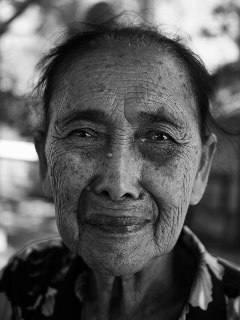 A close black-and-white portrait with soft light across the face and foliage blurred behind.