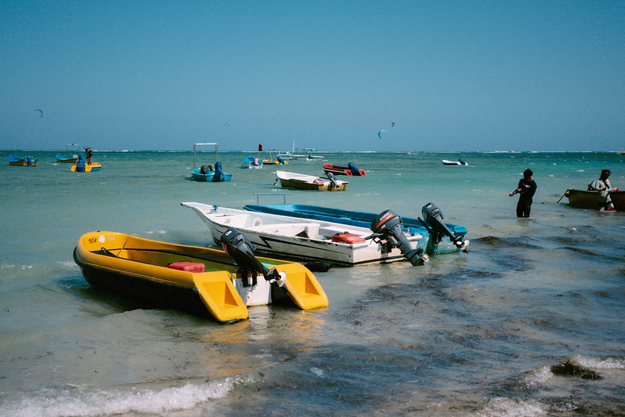 A yellow boat rests beside white and blue boats in clear, shallow coastal water in Bali.