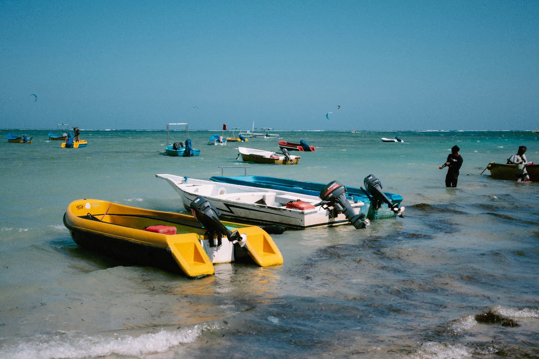 Outboard motors rise above a cluster of colourful boats in shallow water off a Bali beach.