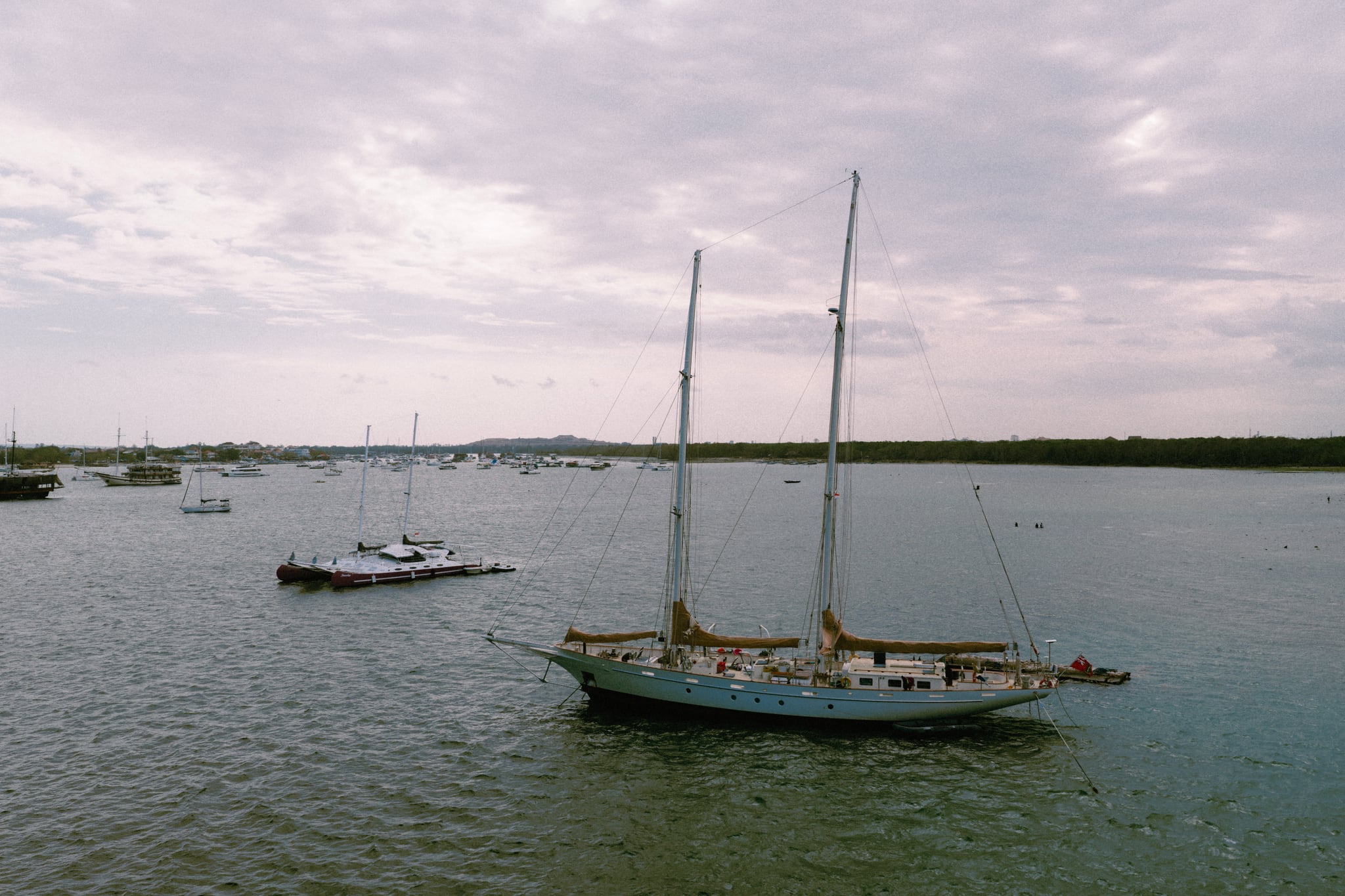 A two-masted sailing boat lies on calm water beneath a soft pink-grey sky in Bali.