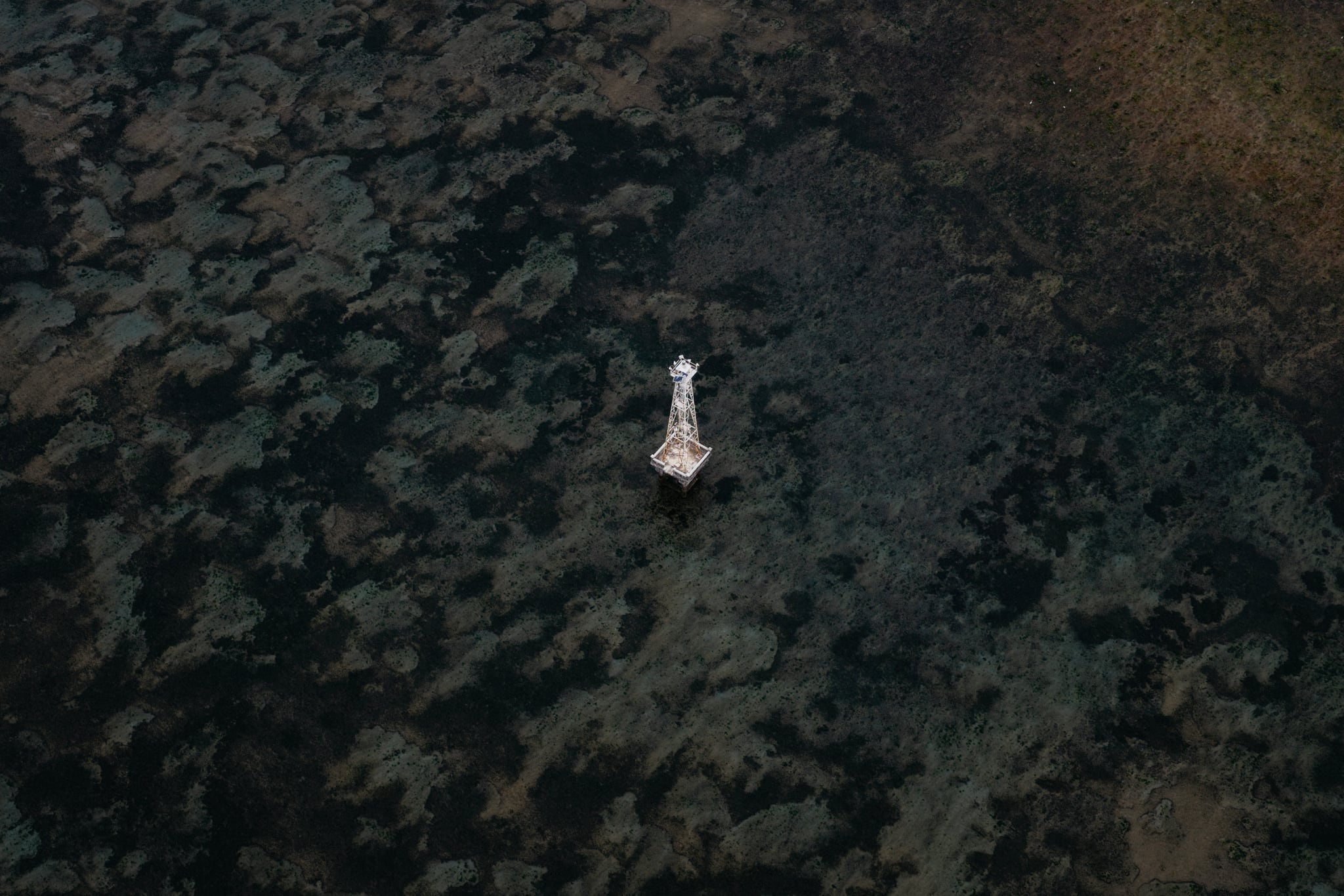 A small white boat sits above a dark, mottled reef in an overhead coastal photograph from Bali.