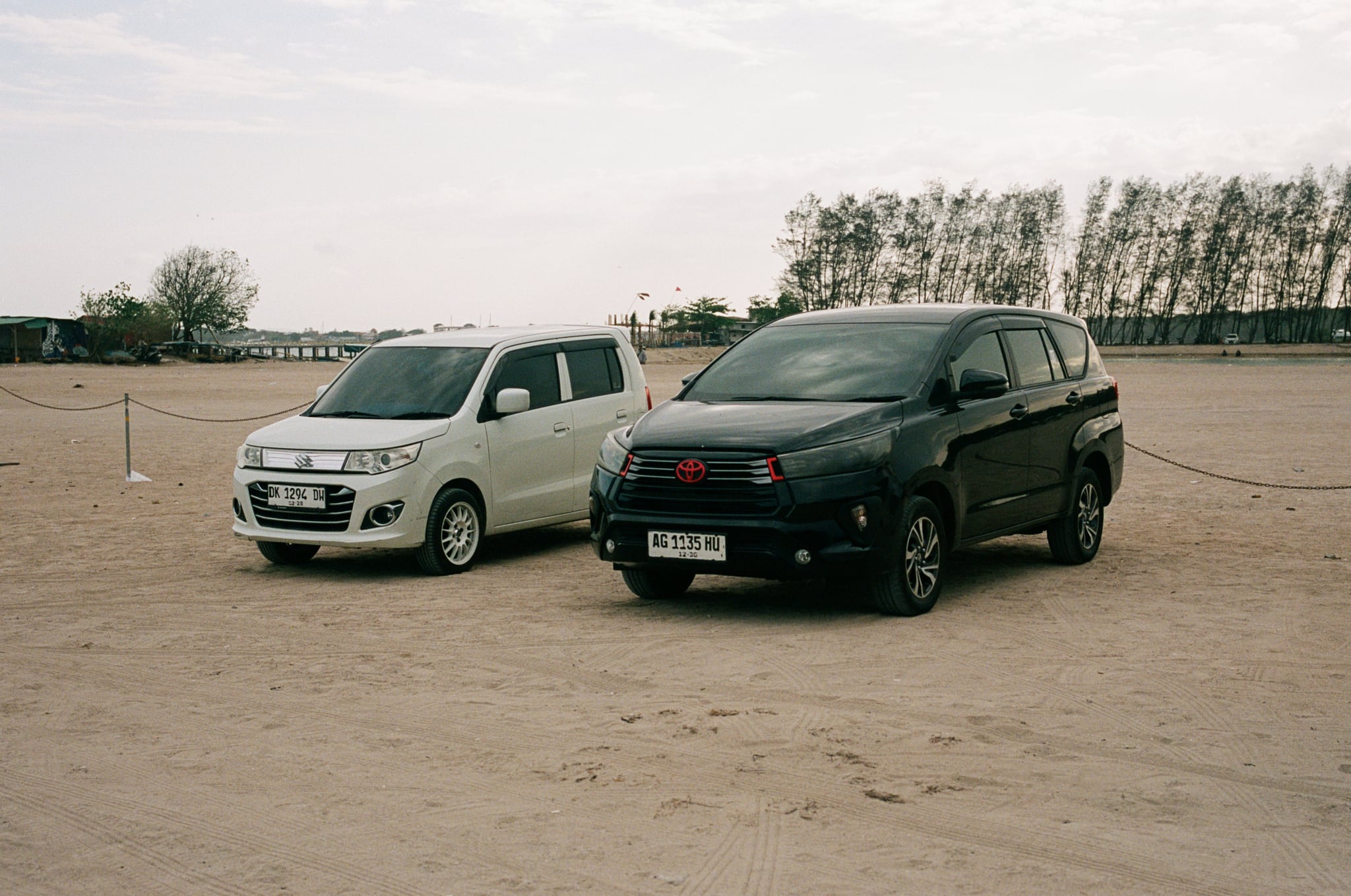 A white van and a dark van stand side by side on broad, sandy open ground.