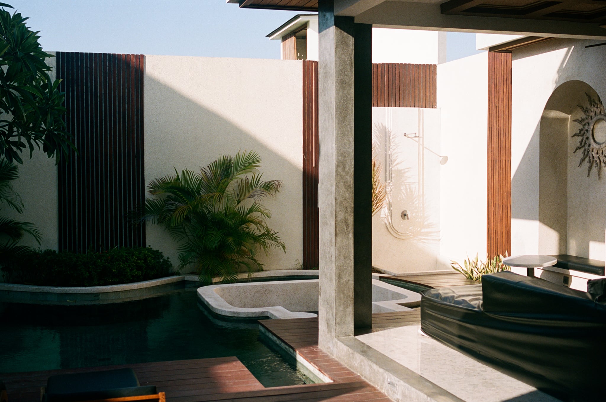 Deep shadows divide a bright courtyard with pale walls, steps, and potted plants.