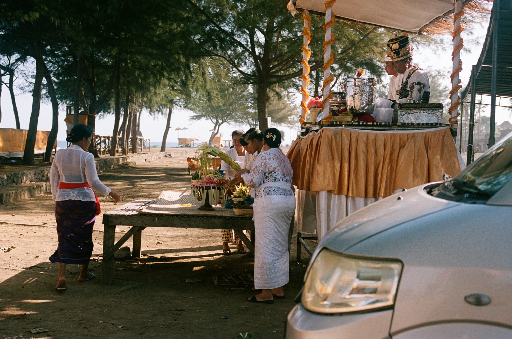 People stand beside a yellow-draped canopy near a parked van and coastal trees.