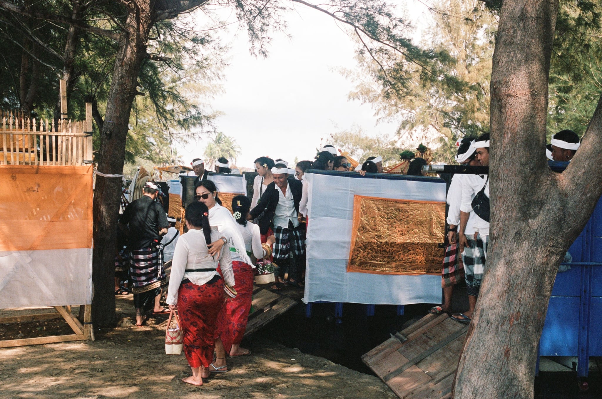 People in white and patterned clothing walk between fabric screens beneath trees.