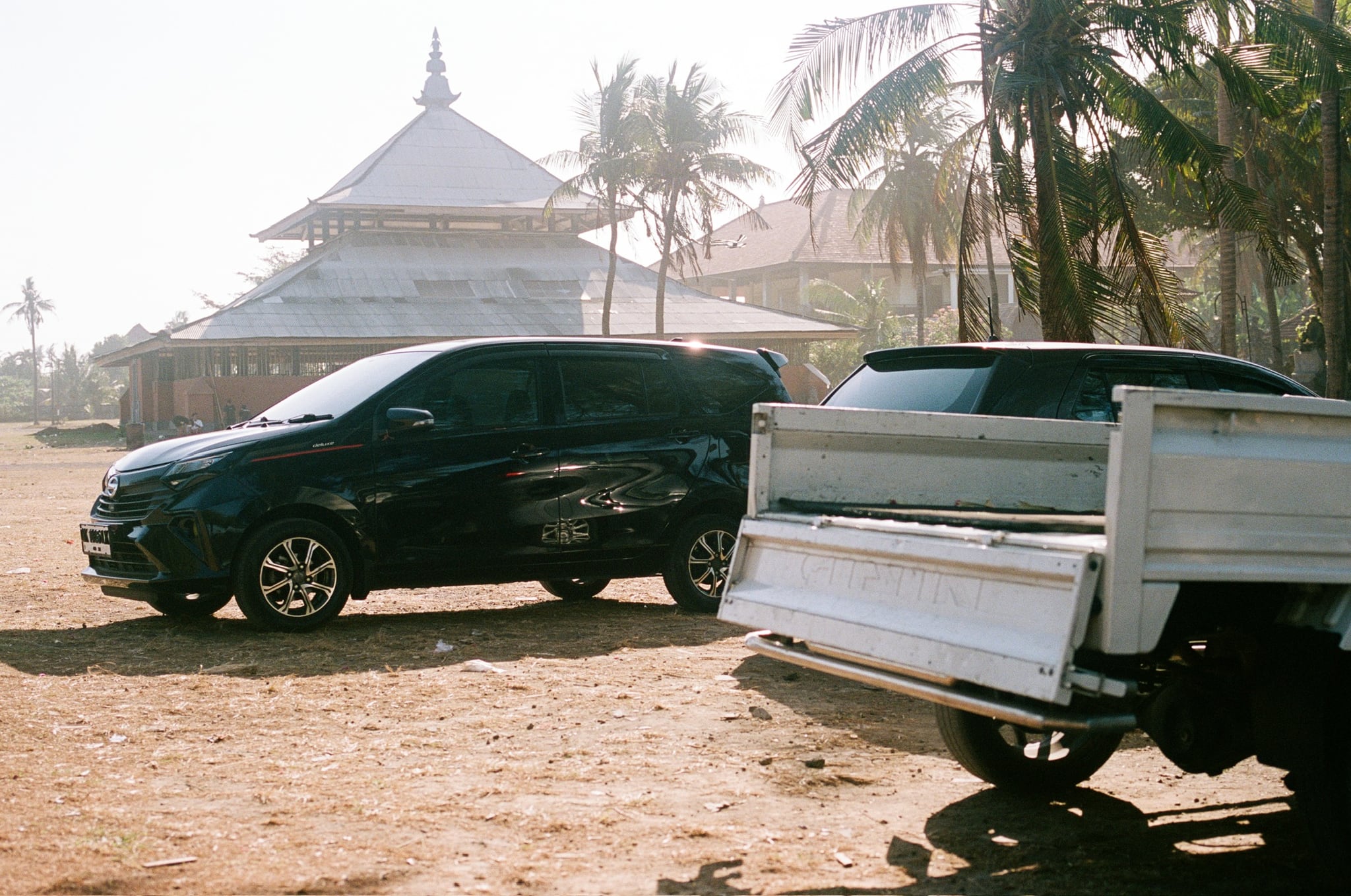 A dark car and a pale pickup are parked beside a pavilion with a broad, tiered roof.