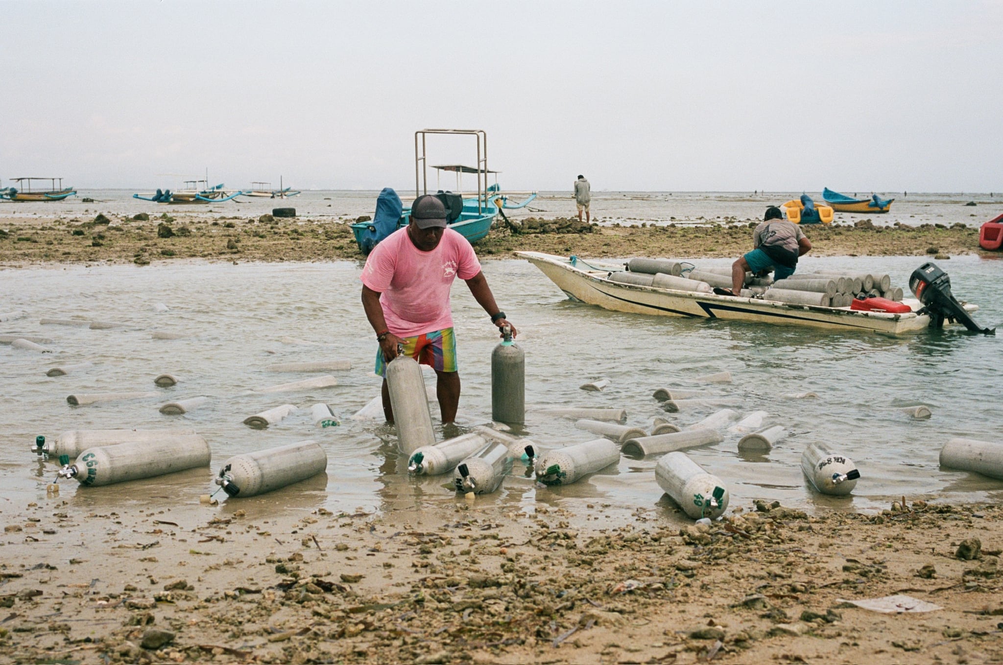 A person in a pink shirt steps through shallow water beside a narrow outrigger boat.