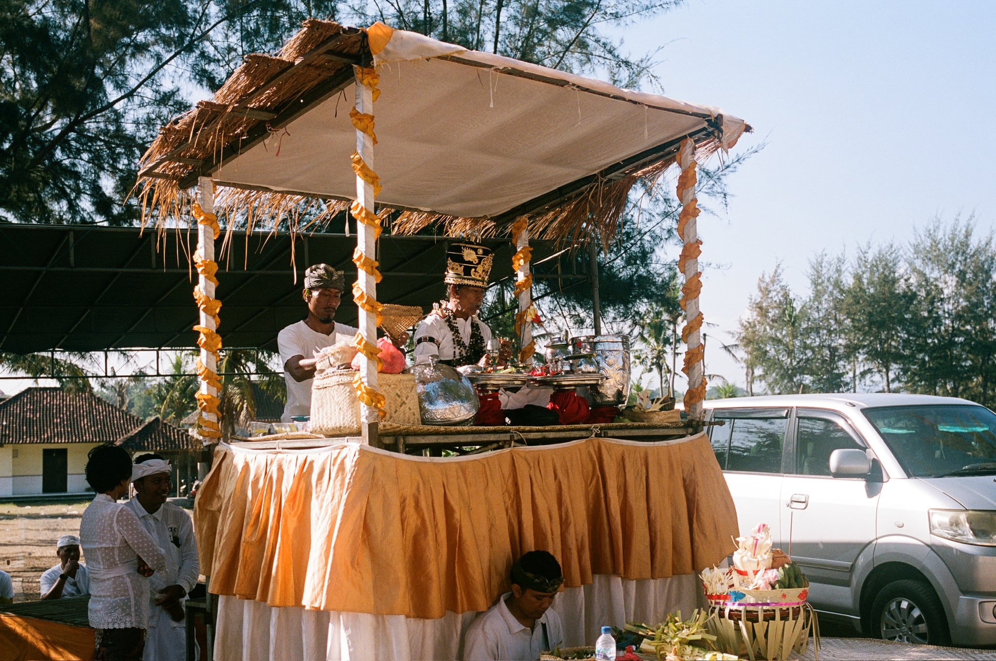 A decorated canopy draped in yellow fabric stands beside parked vehicles under a bright sky.