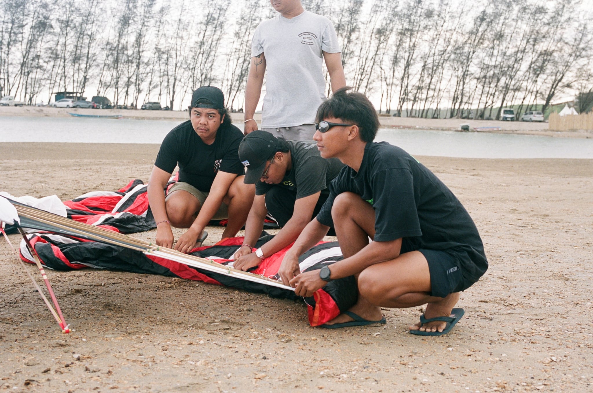 Several people kneel close together while working on a large red-and-white kite.
