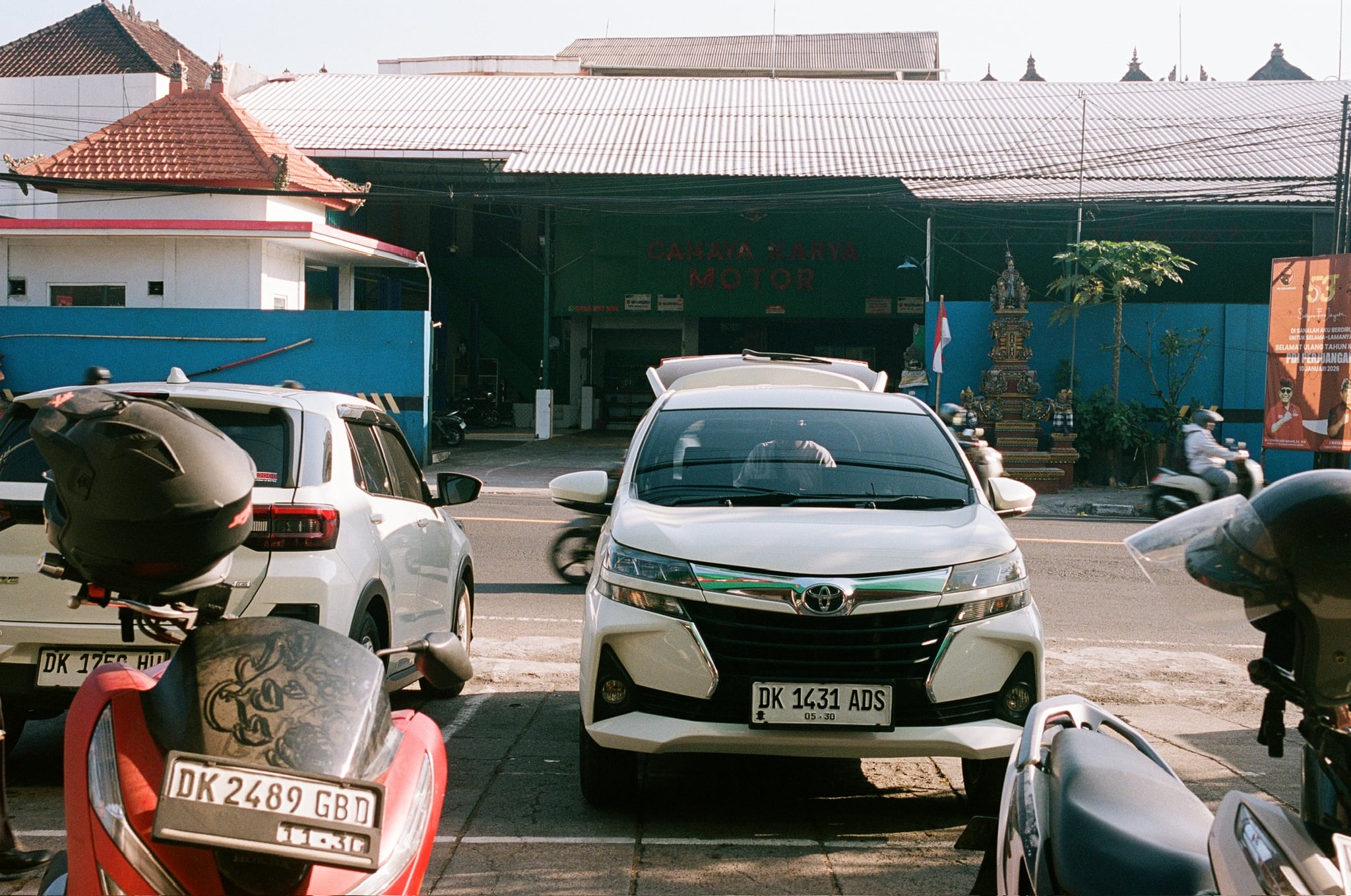 Parked scooters and cars crowd the foreground of low roadside buildings.
