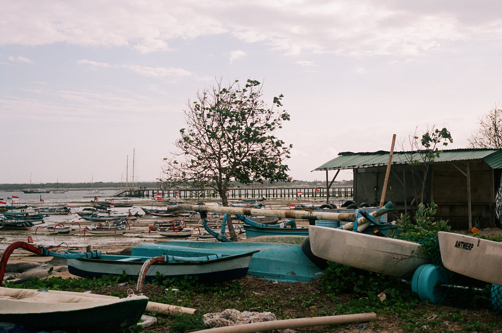 Small boats lie beside a shallow shoreline and a modest waterside shelter.