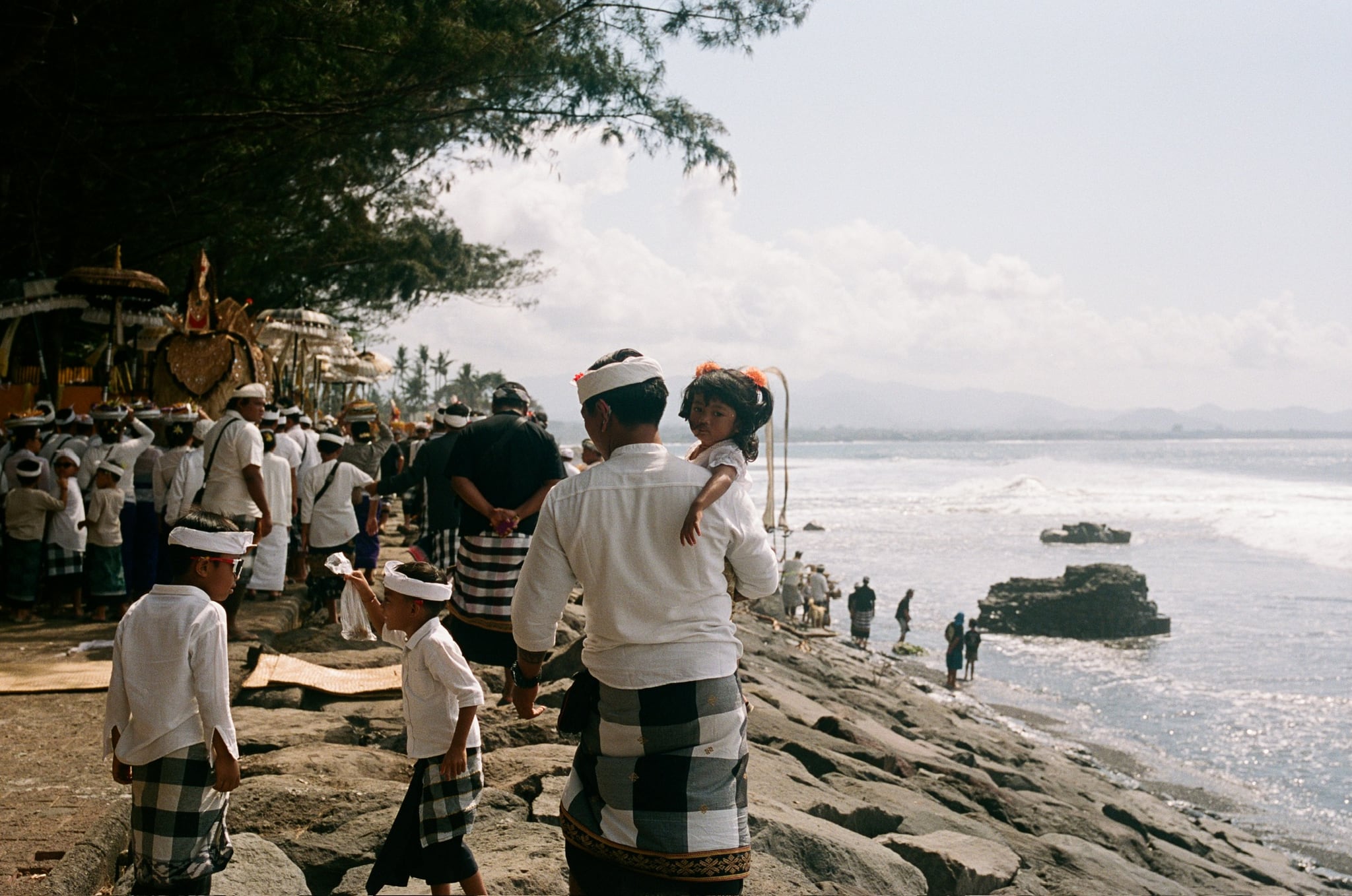 A group in pale clothing stands along a stone sea wall above breaking waves.