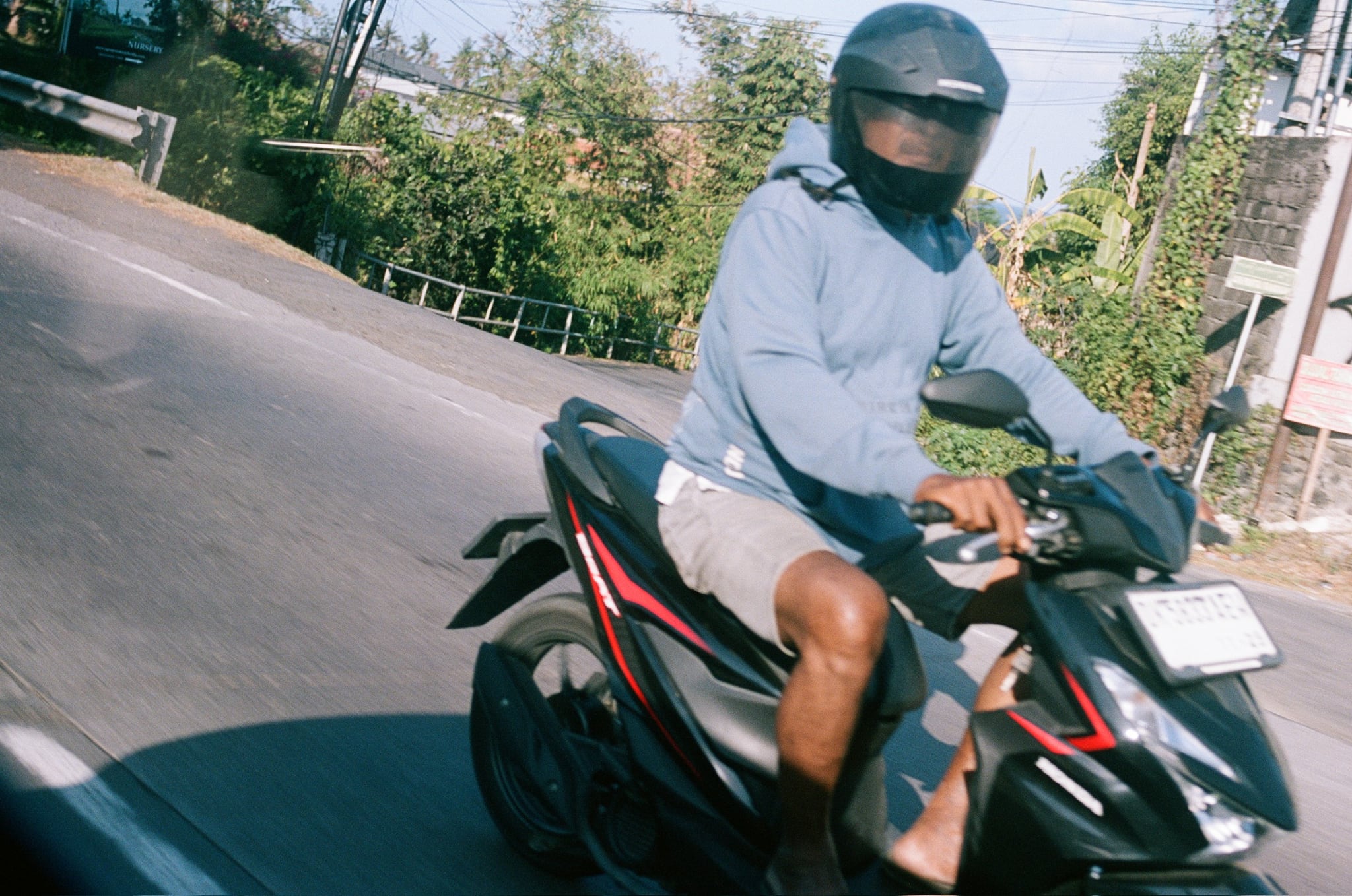 A helmeted rider in a pale top passes close to the camera on a dark scooter.