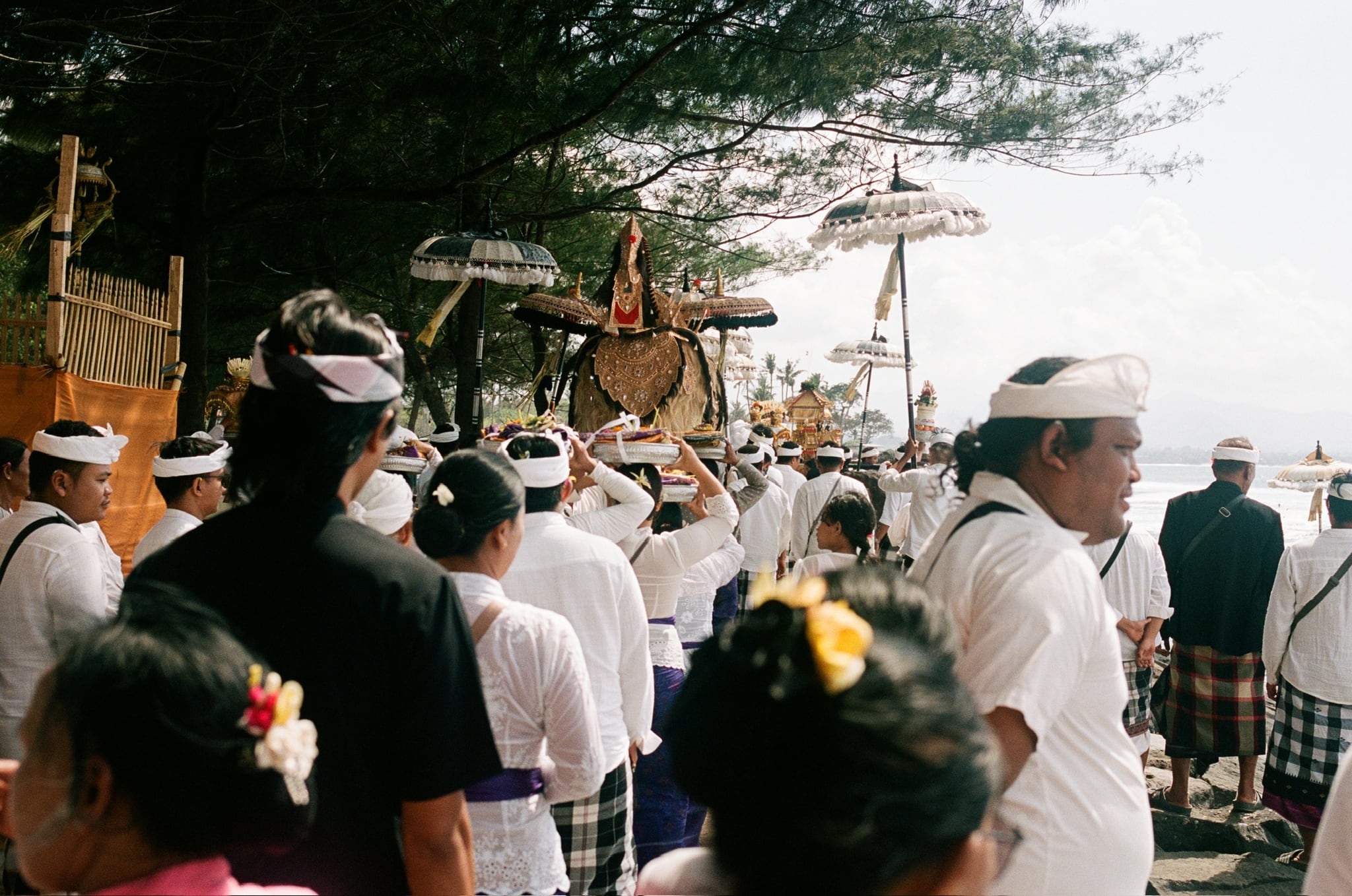 A close view of a coastal gathering with white headwear, flowers, and tall decorated umbrellas.