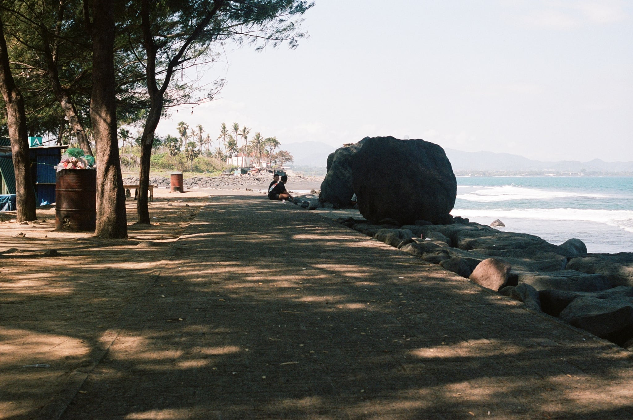 A large dark boulder stands beside a shaded coastal path above the sea.