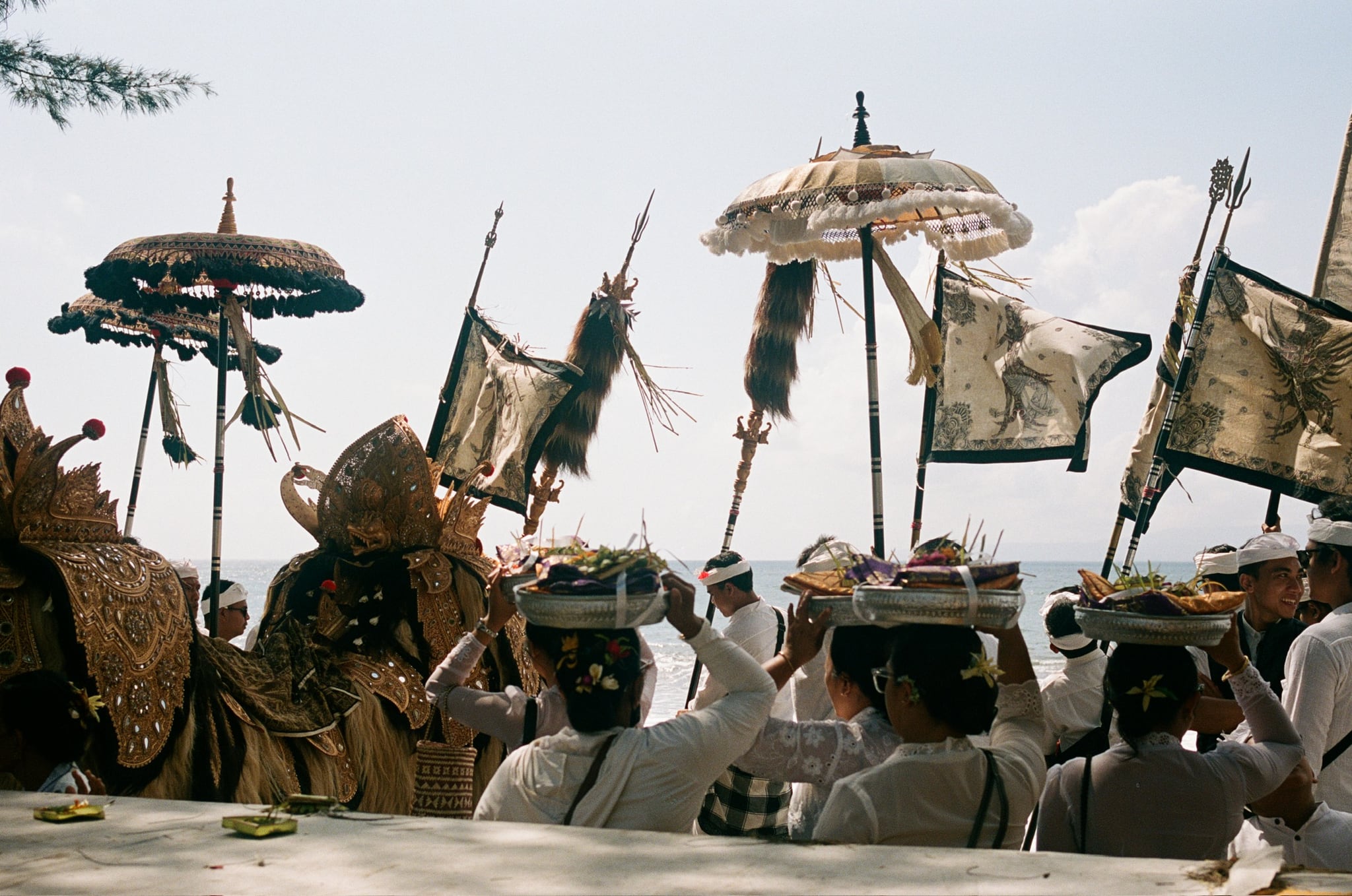 Decorated umbrellas and banners rise above a crowd facing the bright sea.
