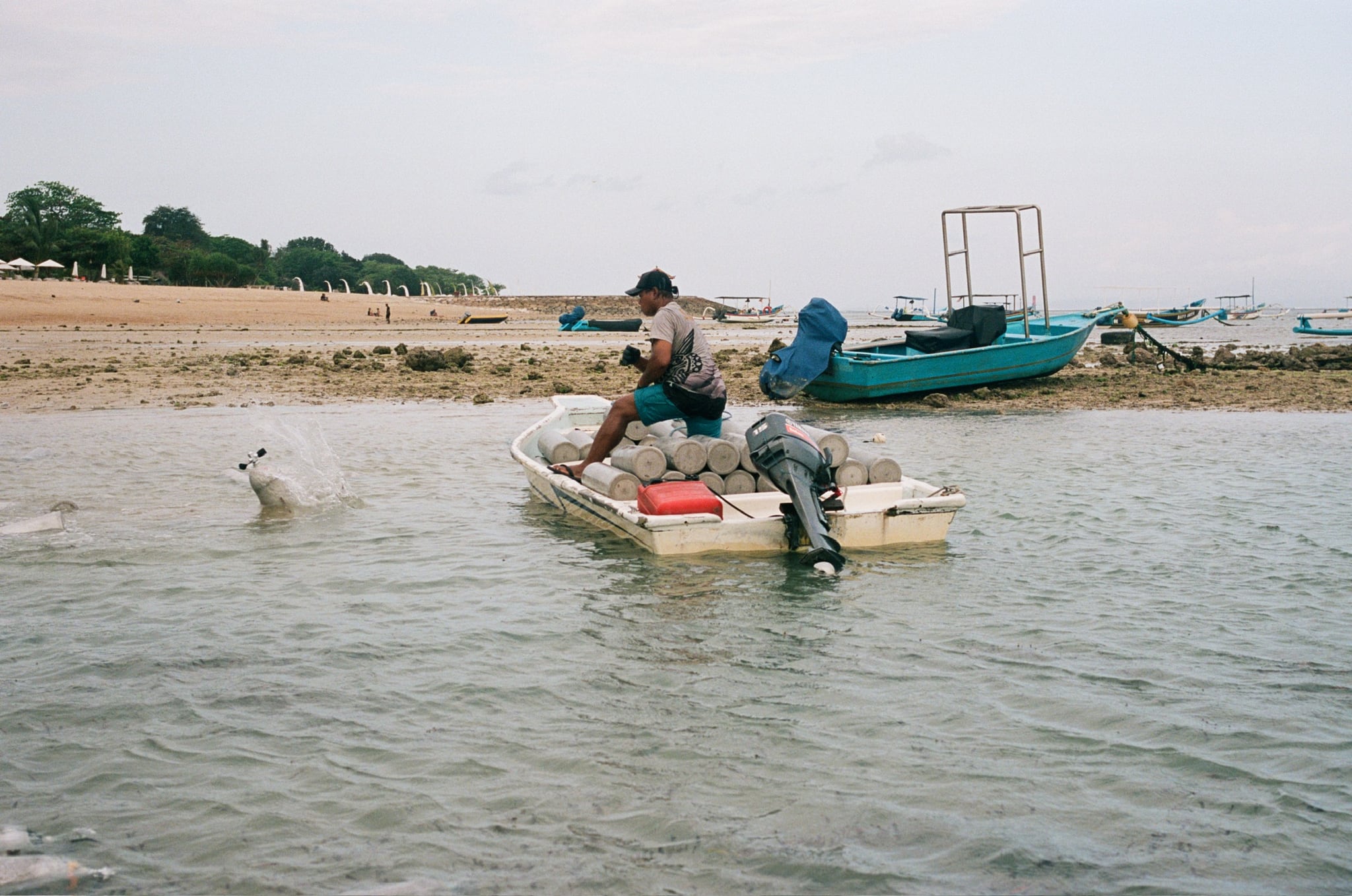 People prepare a small motorboat beside an outrigger in shallow coastal water.