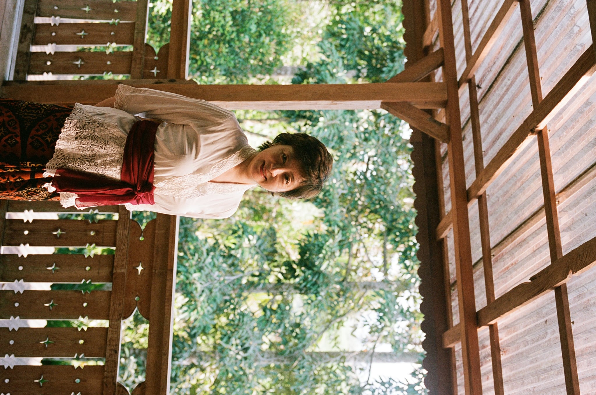 A sideways-framed portrait shows a person in pale clothing on a wooden veranda among trees.