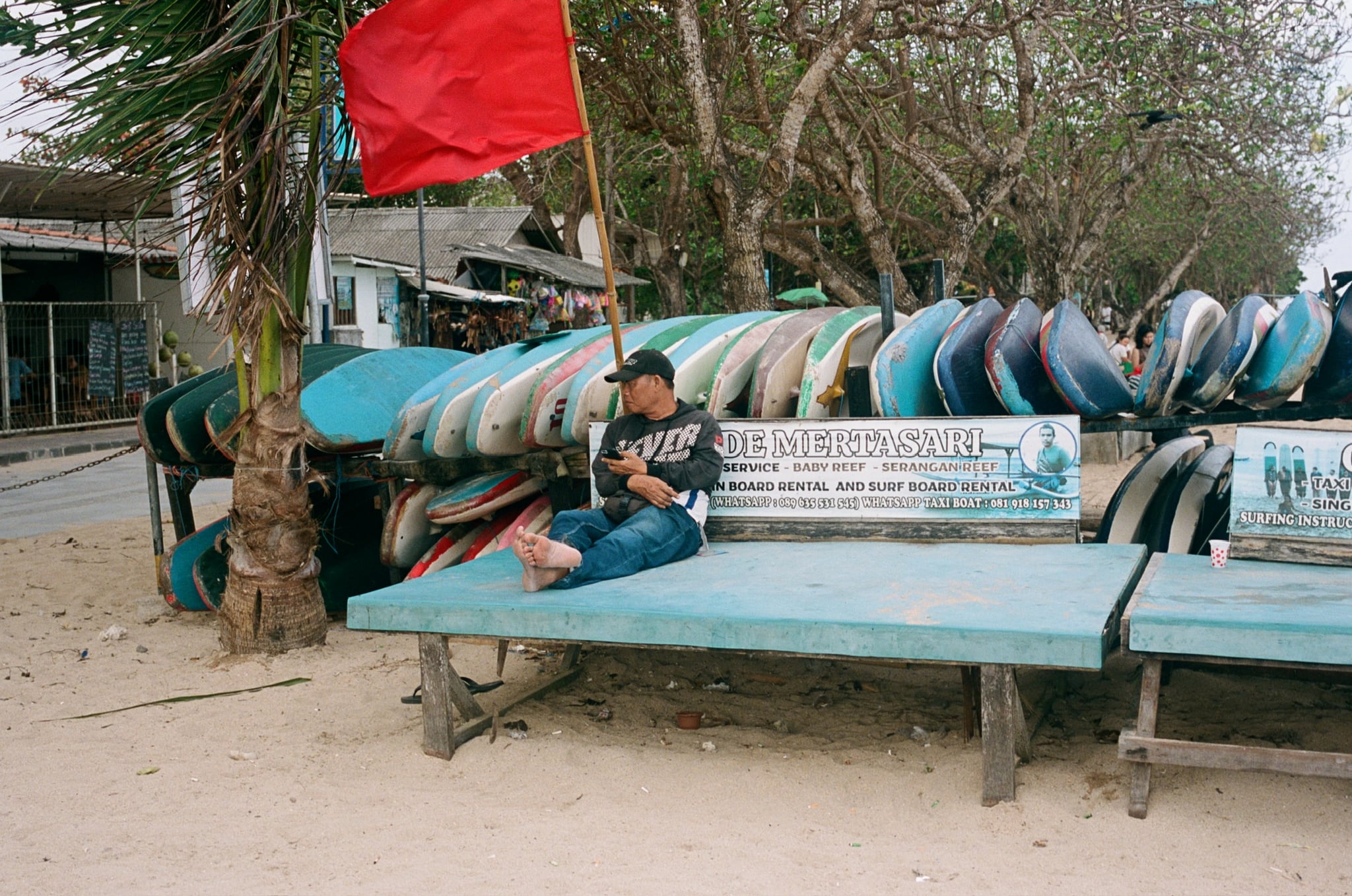 A person sits on a long bench beside stacked colourful boards and a red flag.