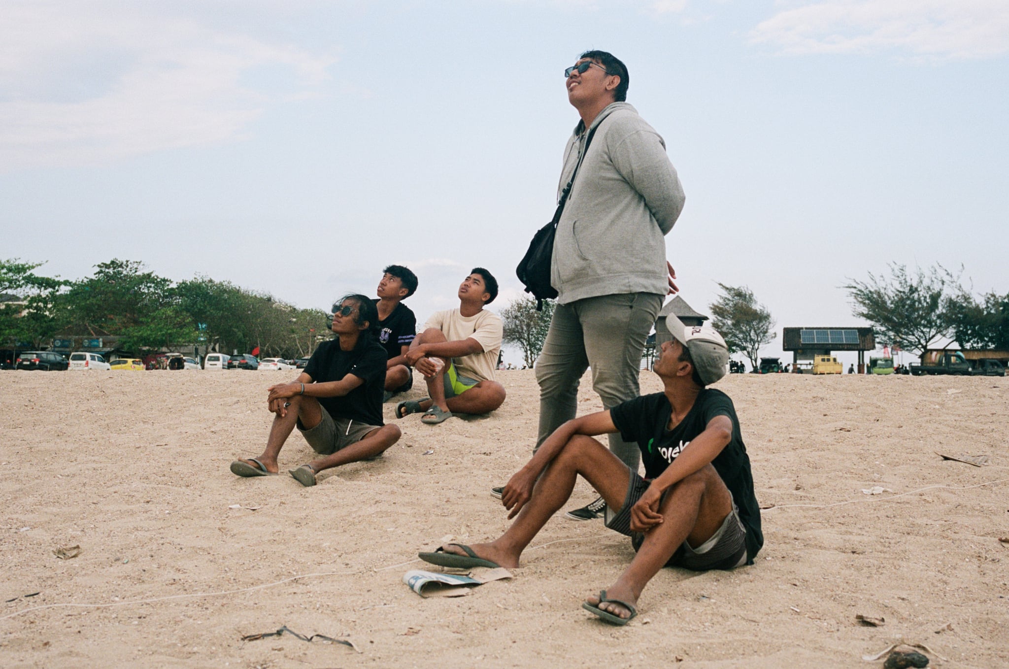 People sit on open ground while a standing figure looks upward beside them.