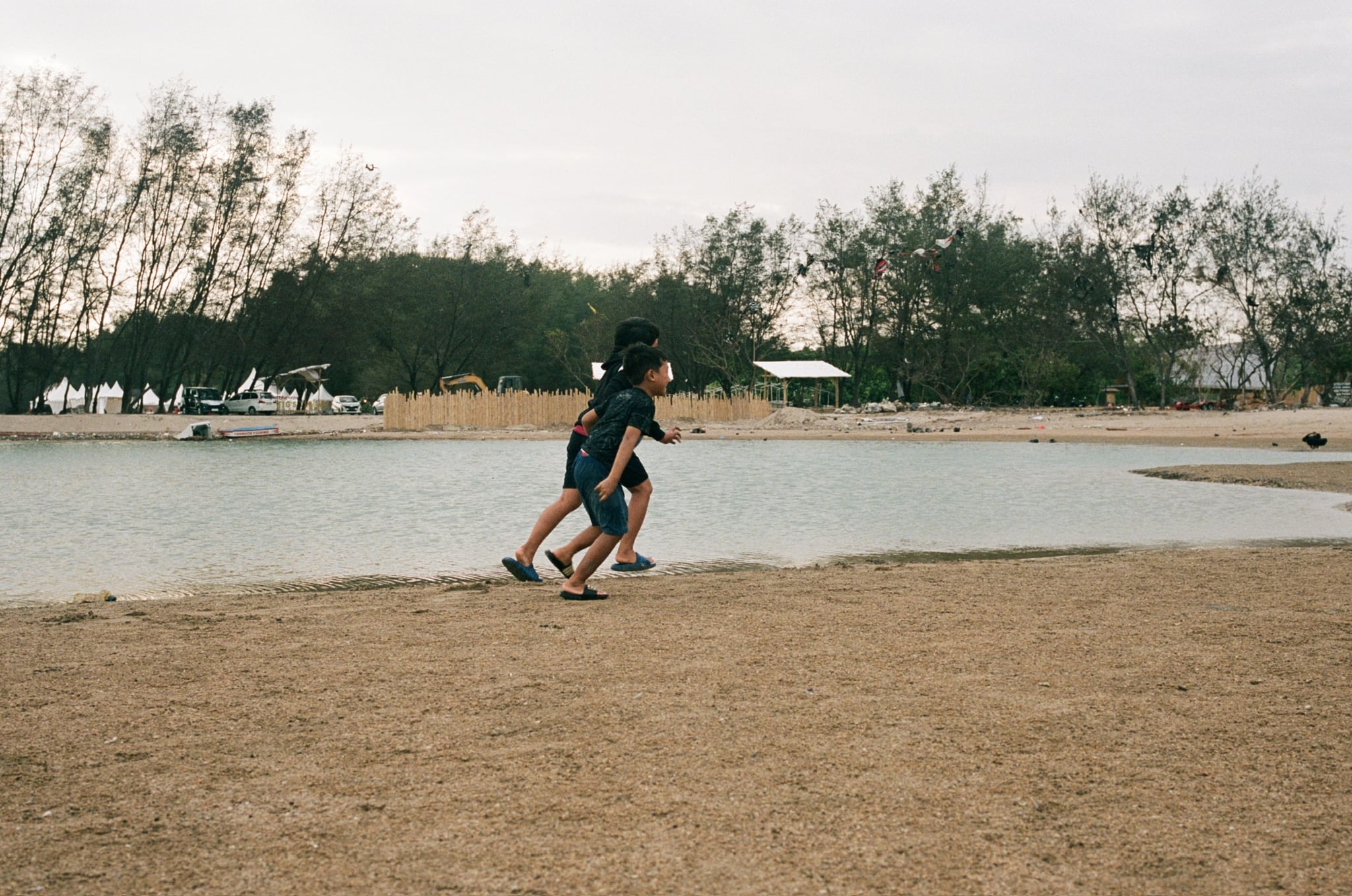 Two people run across dry open ground toward a line of distant trees.